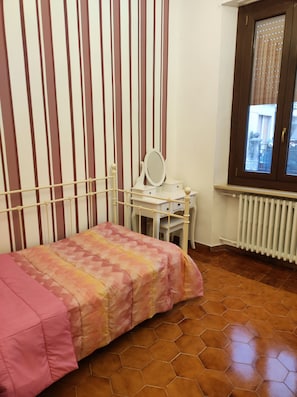 A bedroom with a bed, a desk with a mirror, a radiator, and a window with blinds. - 5 MINUTES FROM THE STATION AND DOWNTOWN (Alessandria)