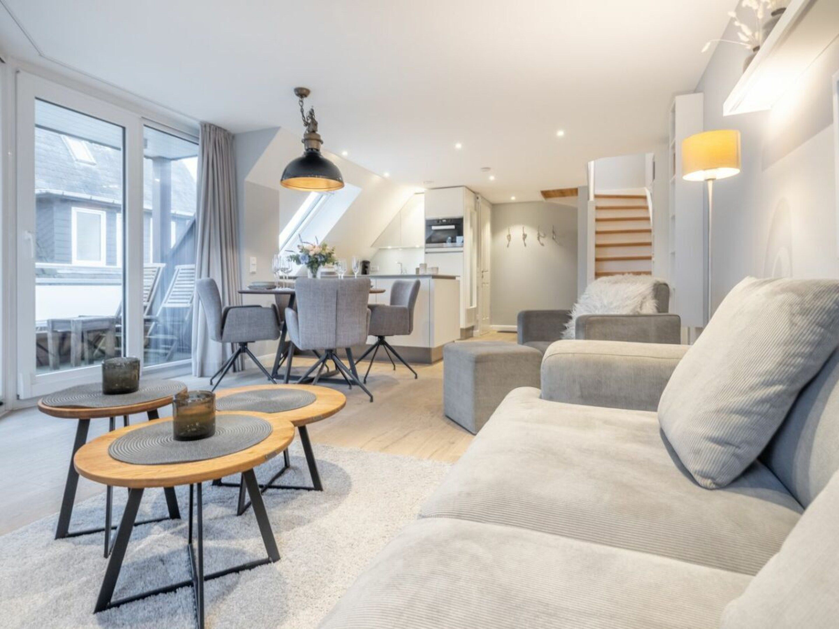 Een moderne woonkamer met een bank, twee ronde tafels en een eethoek met stoelen.