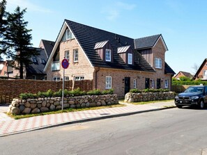 Ein zweistöckiges Haus mit Naturstein-Fassade, einem schwarzen Dach und einer Auffahrt mit geparktem Auto.