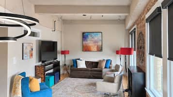 Ein modernes Wohnzimmer mit einer Couch, Sesseln, einem Fernseher und einem Essbereich mit Tisch und Stühlen.