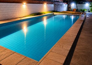 Ein rechteckiger Swimmingpool mit gefliesten Wänden und einer ihn umgebenden Holzterrasse.