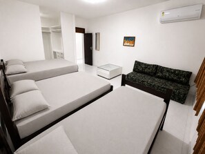Ein modernes, minimalistisches Schlafzimmer mit zwei Einzelbetten, einem kleinen Tisch, einer Couch und einem Kleiderschrank.