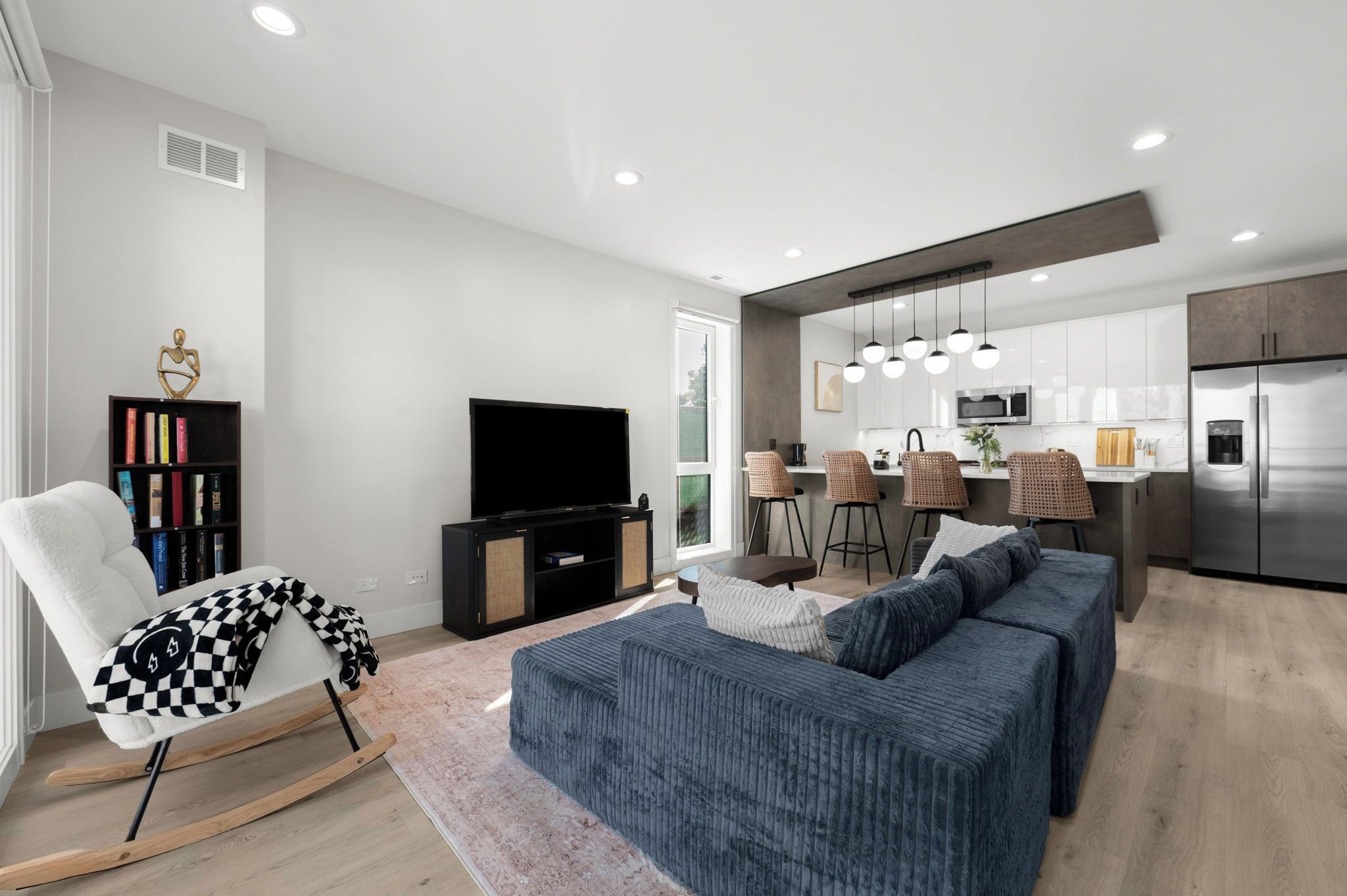 A modern living room with a sofa, a television, a bookshelf, and a dining area with bar stools.