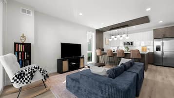 A modern living room with a sofa, a television, a bookshelf, and a dining area with chairs.