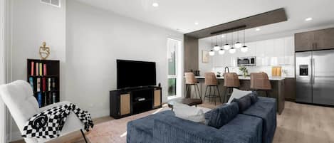 Ein modernes Wohnzimmer mit einer Couch, einem Fernseher, einem Bücherregal und einem Essbereich mit Stühlen.