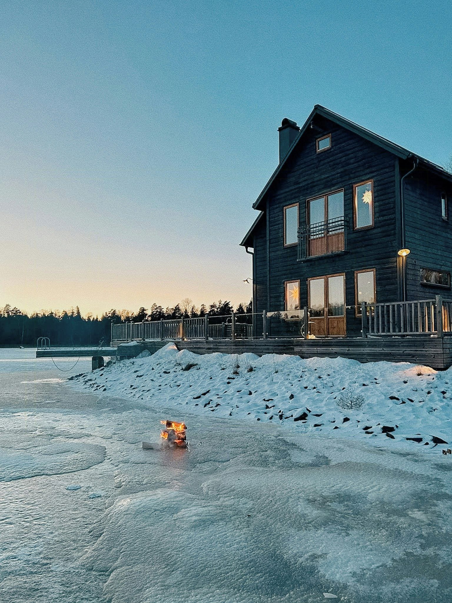 Une grande maison en bois sombre, dotée de nombreuses fenêtres et d’un balcon, entourée de neige.