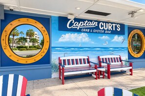 A beach-themed mural with a sign for 'Captain CURT'S CRAB & OYSTER BAR' and two striped beach chairs. - Renovated + New Furniture, Bayfront Resort Class Amenities, Walk to Siesta Beach (Siesta Key)