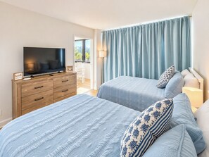 A bedroom with two beds, a TV, a wooden dresser, and a window with curtains. - Renovated + New Furniture, Bayfront Resort Class Amenities, Walk to Siesta Beach (Siesta Key)