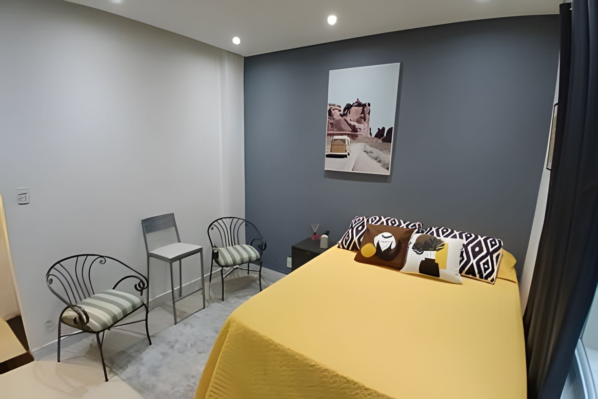 Un dormitorio con cama, dos sillas, una mesita y un cuadro colgado en la pared.