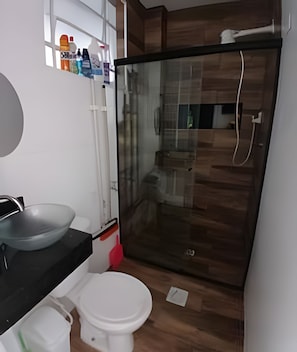 Un baño moderno con cabina de ducha de vidrio, inodoro blanco y encimera negra con lavamanos de vidrio.