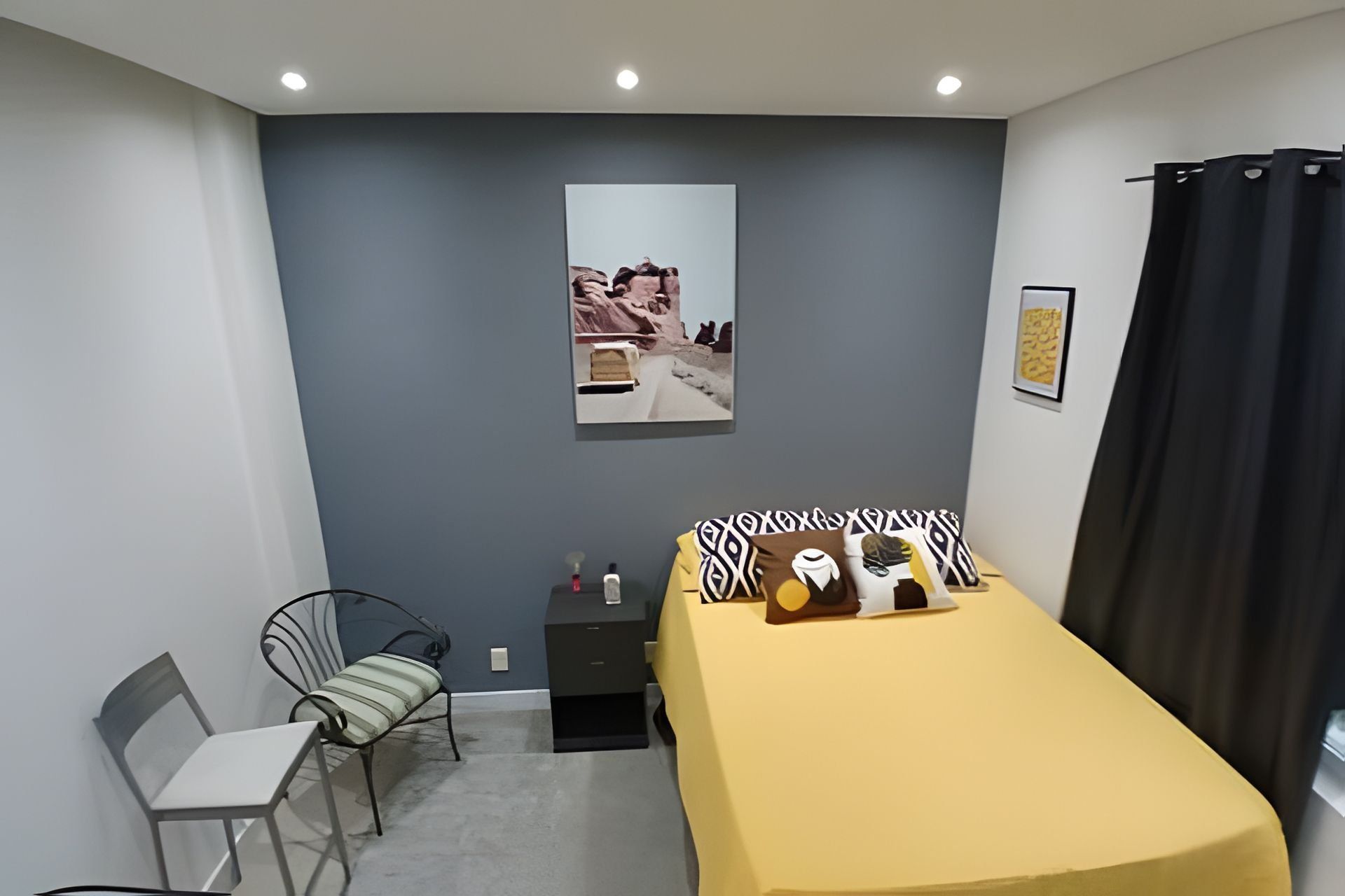 Une chambre à coucher avec un lit, une chaise, une petite table et un tableau accroché au mur.