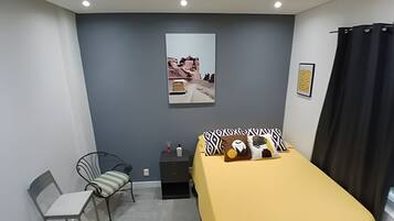 Une chambre à coucher avec un lit, une chaise, une petite table et un tableau accroché au mur.
