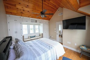 A bedroom with a bed, a ceiling fan, a window, built-in cabinets, and a mounted TV. - Cozy Lake House on Lake Erie (Bay Village)