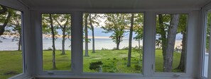 A room with a large window offering a view of a grassy area and trees. - Cozy Lake House on Lake Erie (Bay Village)