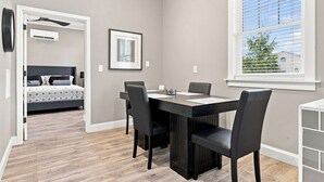 Une pièce comprenant une table à manger, des chaises, un lit et une fenêtre avec des stores.