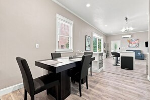 A modern dining area with a black table and chairs, a kitchen in the background, and a living area with a sofa and a TV.