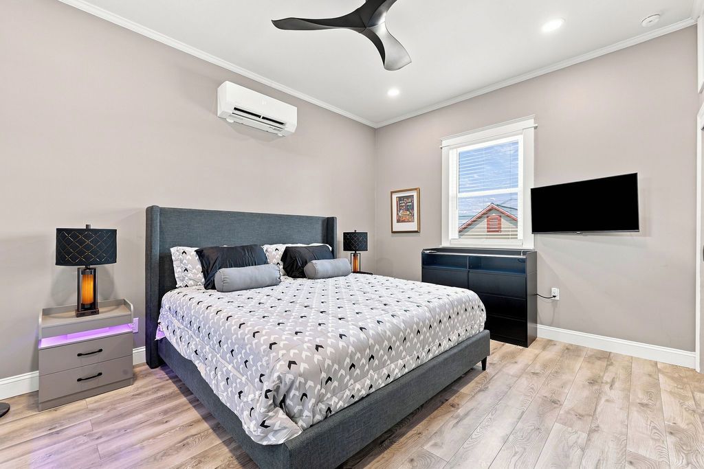 A modern bedroom with a bed, bedside tables, a ceiling fan, an air conditioning unit, a window, and a television.