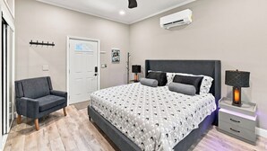 Une chambre à coucher comprenant un lit, une chaise, une table de chevet avec une lampe, un ventilateur de plafond et un appareil de climatisation.