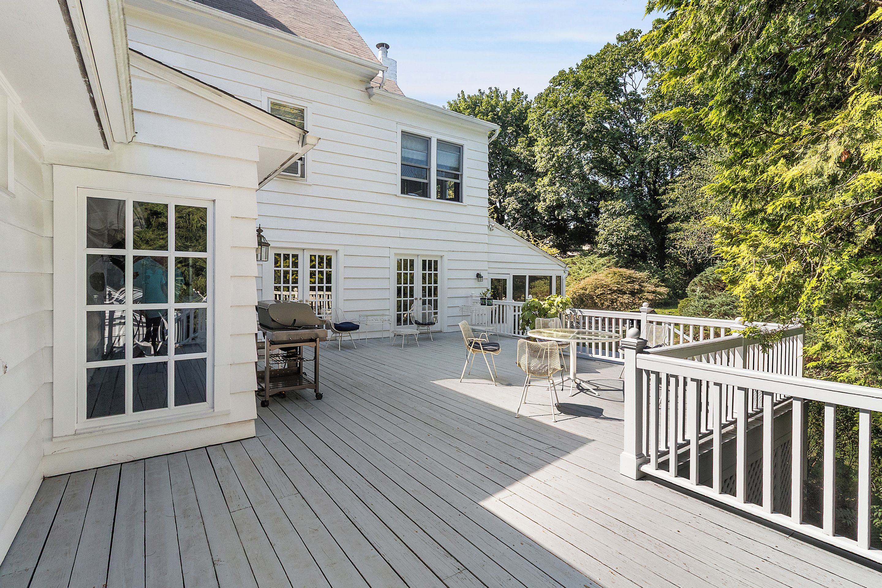 A white two-story house with a deck, outdoor furniture, and a barbecue grill.