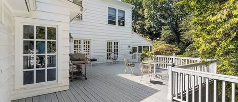 A white two-story house with a deck, outdoor furniture, and a barbecue grill.