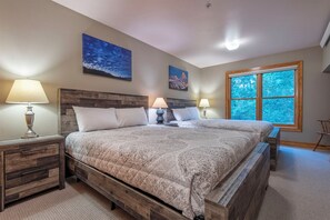 A bedroom with a large bed, wooden headboard, two bedside tables with lamps, and a window with a view of trees.