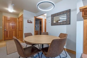A dining area with a round table and six chairs, a wooden door, a mirror, and a ceiling light fixture.