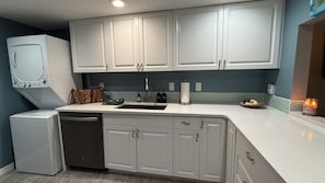 Una cocina con armarios blancos, lavavajillas, fregadero y encimera con cesta y botellas.