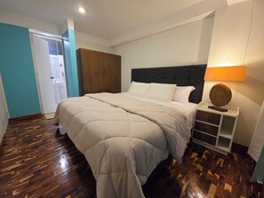A bedroom with a bed, wooden wardrobe, bedside table, and a lamp. - Moderno Depa Familiar de 3BR con Garaje Cerca a San Blas (Cusco)