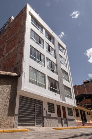 A multi-story building with a garage entrance, large windows, and a brick facade. - Moderno Depa Familiar de 3BR con Garaje Cerca a San Blas (Cusco)