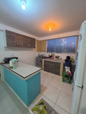 A kitchen with a central island, cabinets, a refrigerator, and a window. - Moderno Depa Familiar de 3BR con Garaje Cerca a San Blas (Cusco)