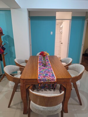 A dining area with a wooden table, six chairs, and a colorful table runner. - Moderno Depa Familiar de 3BR con Garaje Cerca a San Blas (Cusco)