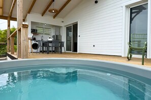 Ein Schwimmbad mit Holzterrasse, eine Küchenzeile mit modernen Geräten und ein grüner Stuhl.