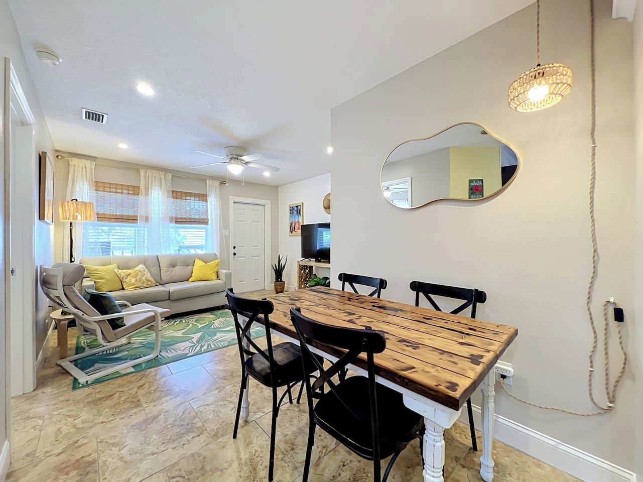 A dining area with a wooden table and black chairs, a sofa with yellow cushions, and a ceiling fan.