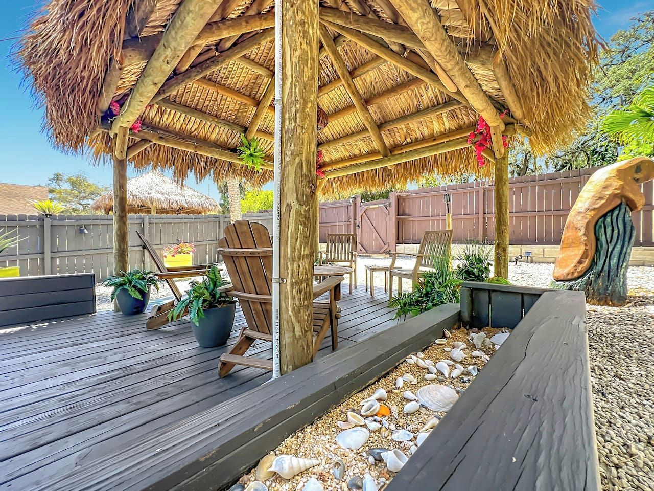 Eine Holzterrasse mit einer reetgedeckten Struktur, Gartenmöbeln und Blumentöpfen.