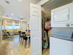 A room with a dining area, a sofa, a table, and a washing machine.