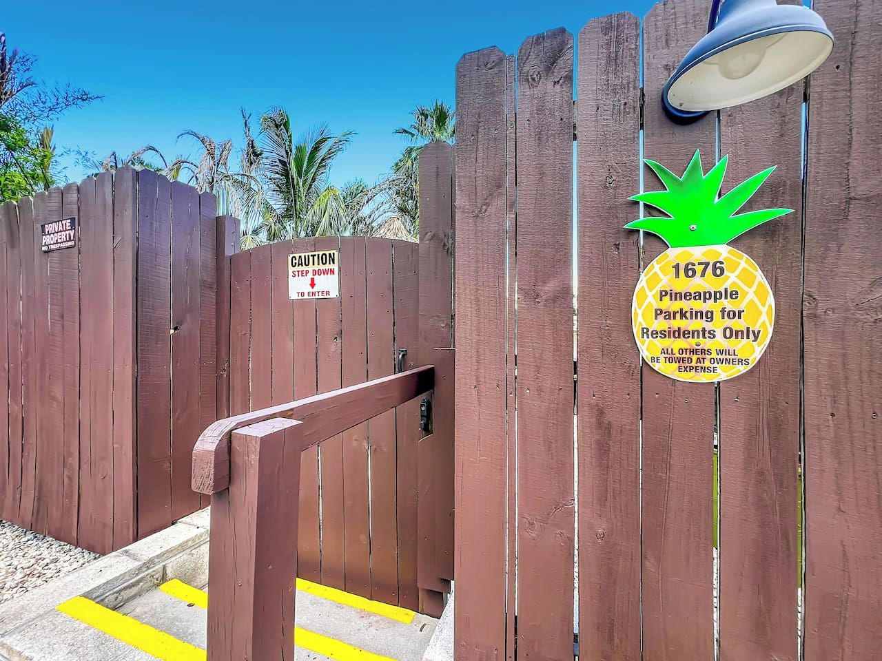 Une porte en bois avec une pancarte indiquant « Propriété privée », une autre pancarte indiquant « Attention, marche » et une troisième pancarte indiquant « Parking réservé aux résidents – 1676 Pineapple ».
