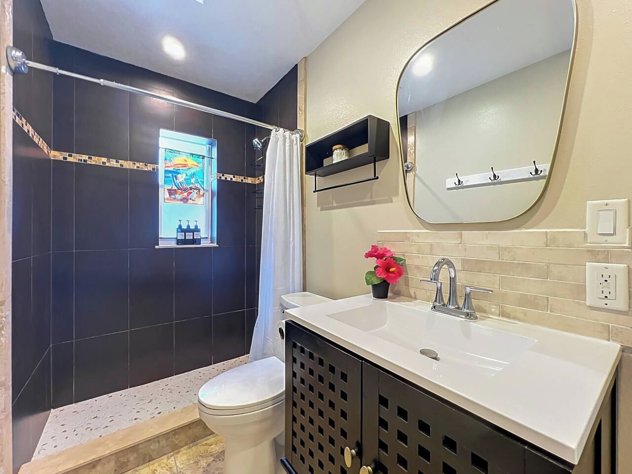 Une salle de bain avec un lavabo blanc, un miroir, un rideau de douche et une petite étagère contenant des articles de toilette.