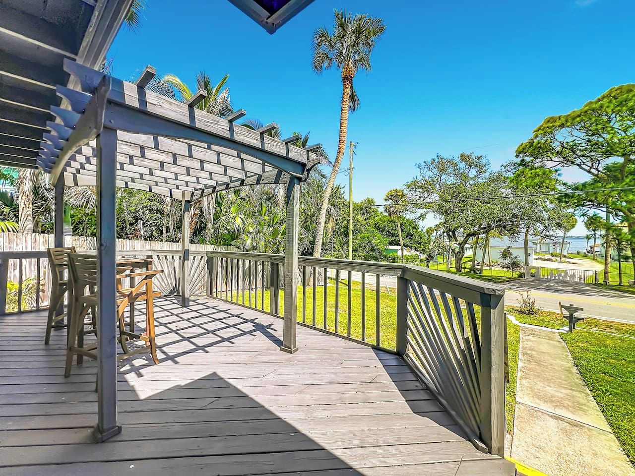 A wooden deck with a pergola, outdoor furniture, and a view of a park with palm trees.