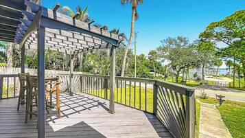A wooden deck with a pergola, outdoor furniture, and a view of a park with palm trees.