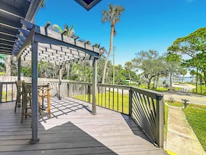 A wooden deck with a pergola, outdoor furniture, and a view of a park with palm trees.