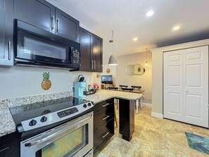 A kitchen with dark cabinets, a microwave, a stove, and a coffee station.