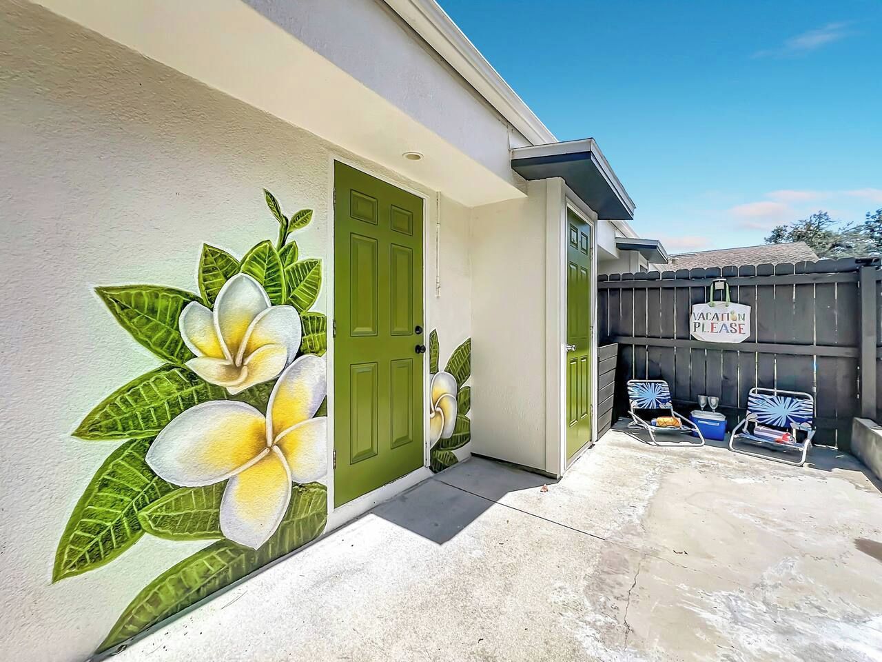 A house with a green door, a patio with two chairs, and a wall mural of flowers.