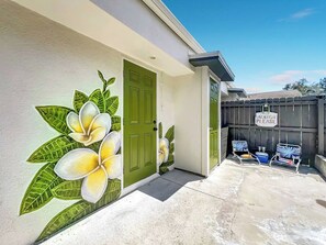 A house with a green door, a patio with two chairs, and a wall mural of flowers.