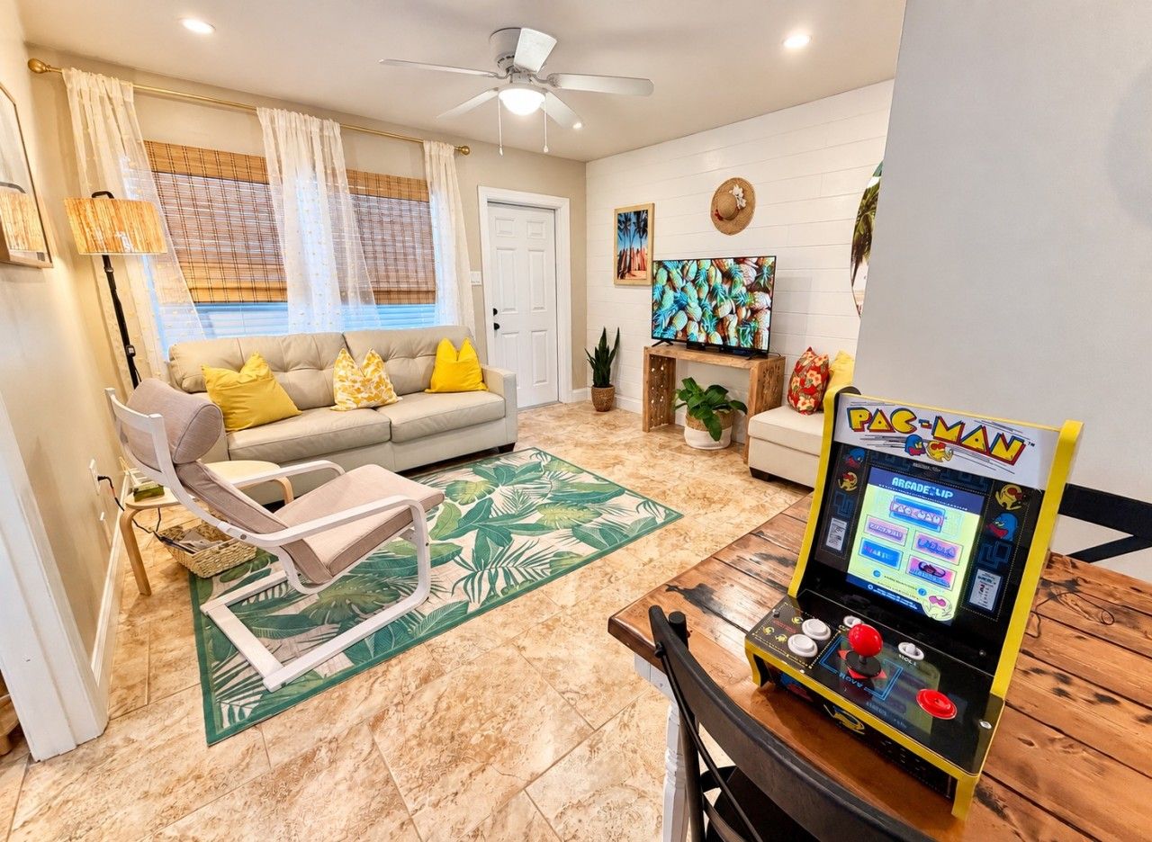 Un salon comprenant un canapé, des fauteuils, une table basse et une borne d’arcade Pac-Man.