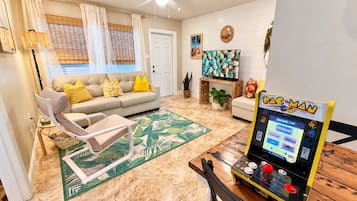 A living room with a sofa, armchairs, a coffee table, and a Pac-Man arcade game.