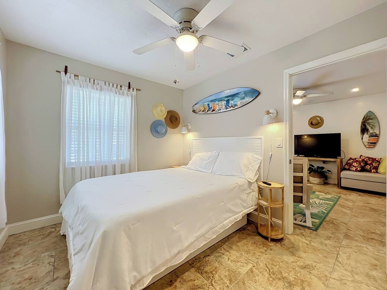 A bedroom with a bed, a ceiling fan, a TV, and a door leading to another room.