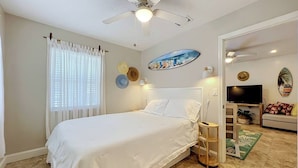 Un dormitorio con cama, ventilador de techo, televisor y puerta que da a otra habitación.