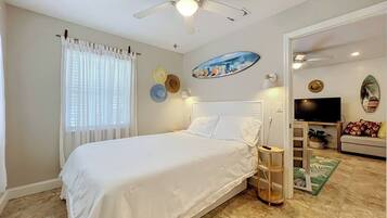 A bedroom with a bed, a ceiling fan, a TV, and a door leading to another room.