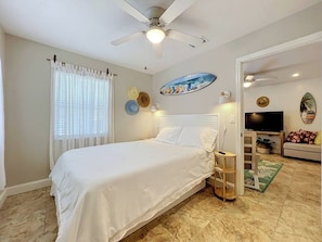 A bedroom with a bed, a ceiling fan, a TV, and a door leading to another room.