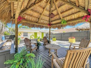 Un patio al aire libre con muebles de madera, techo de paja y plantas en macetas.